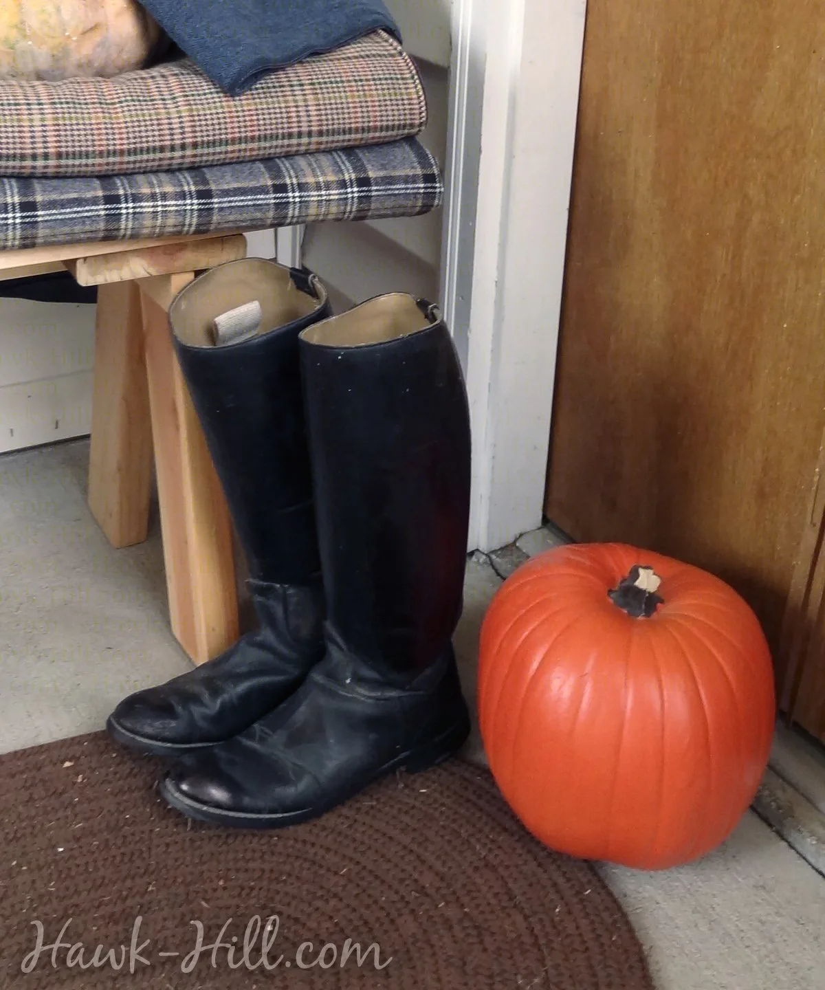 Black boots next to a pumpkin on a porch.