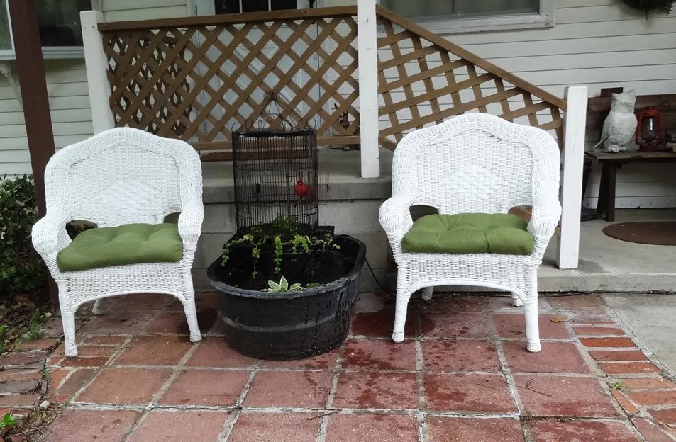 Wicker chairs and birdcage water feature on porch