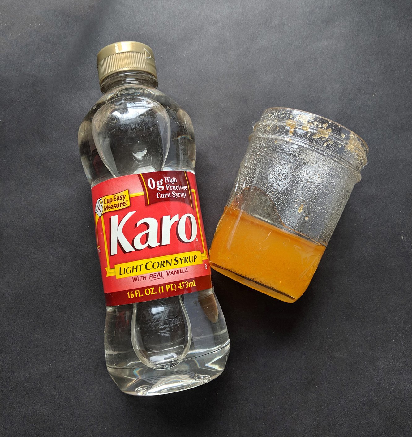 A bottle of karo syrup and a jar of crystallized honey on a black backdrop.