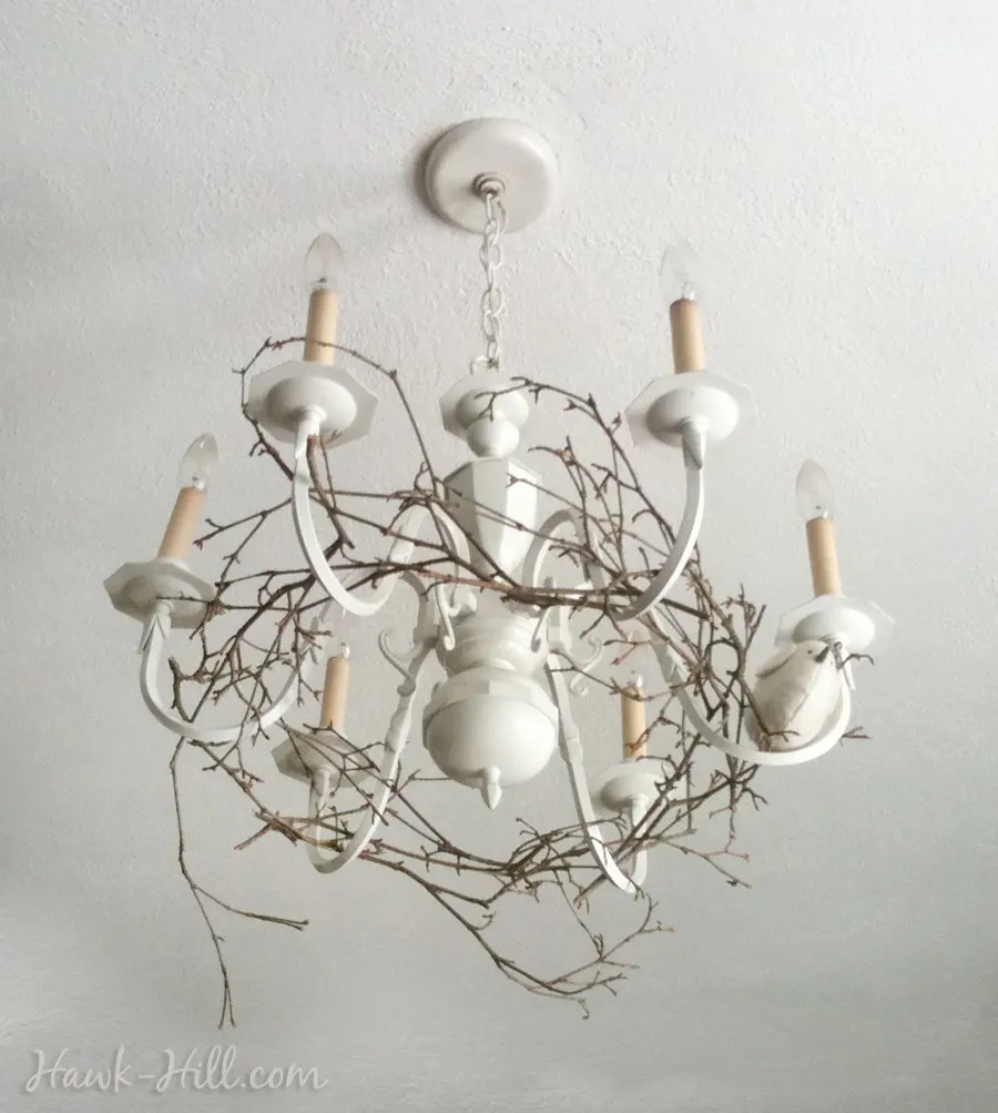 My woodland inspired chandelier upgrade, featuring a wreath of branches and a tiny bird, resting on the chandelier arms. 