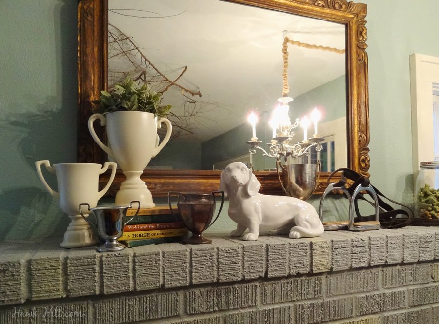 Equestrian fireplace mantle with trophy display, books, and stirrup irons.
