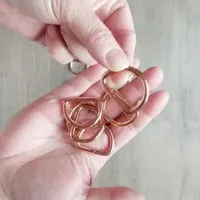 A person's hands hold rose gold D rings.