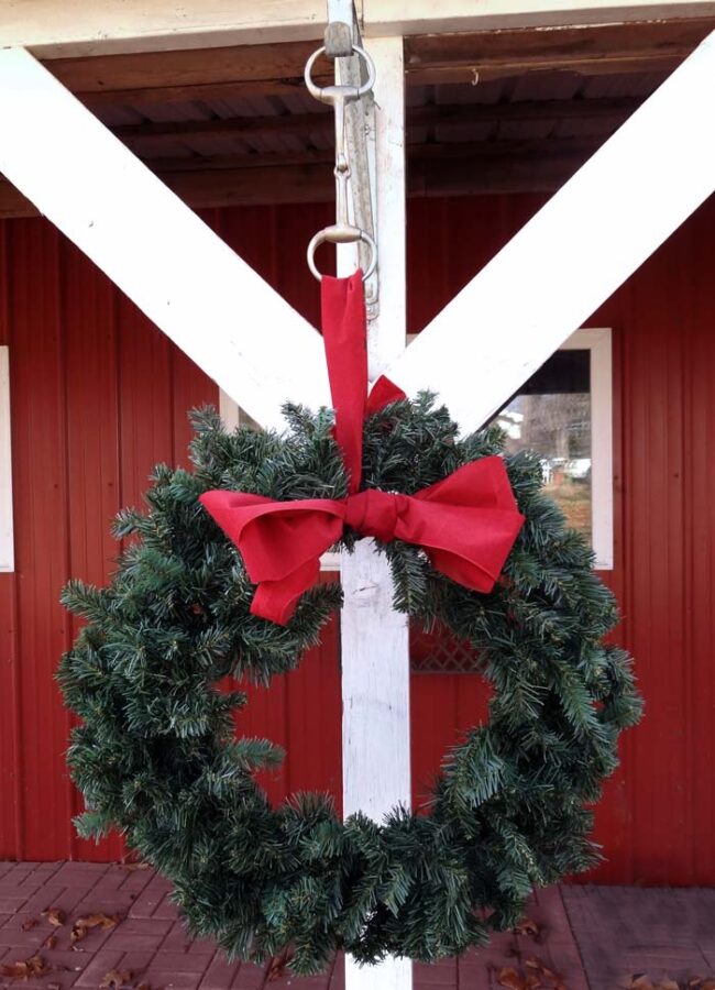 An evergreen reef hanging on the front of a stable with a snaffle bit hanger