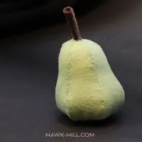 A pale green felt pear on a dark brown background
