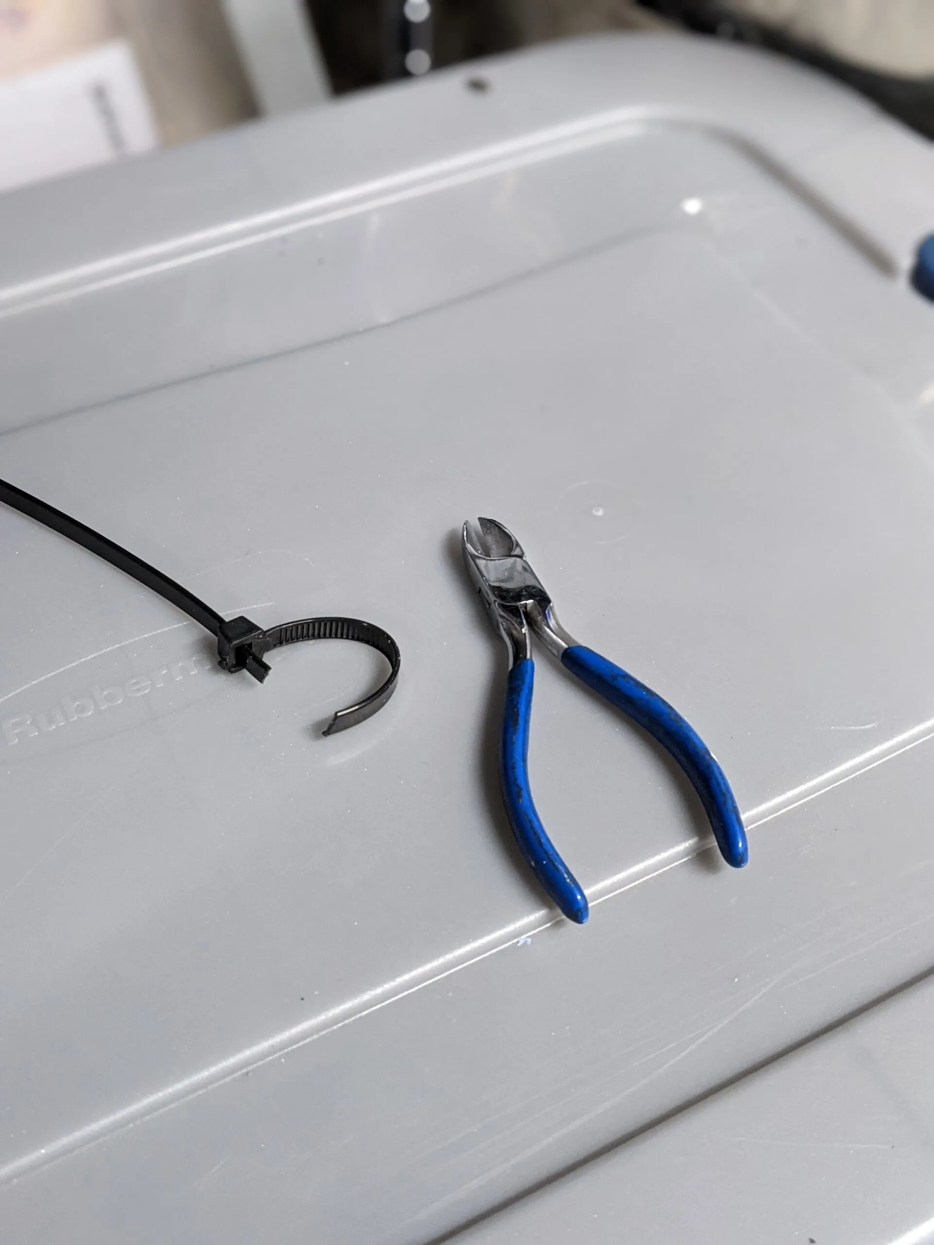 Wire cutter pictured next to a cut heavy duty zip tie, on top of a plastic storage tote.