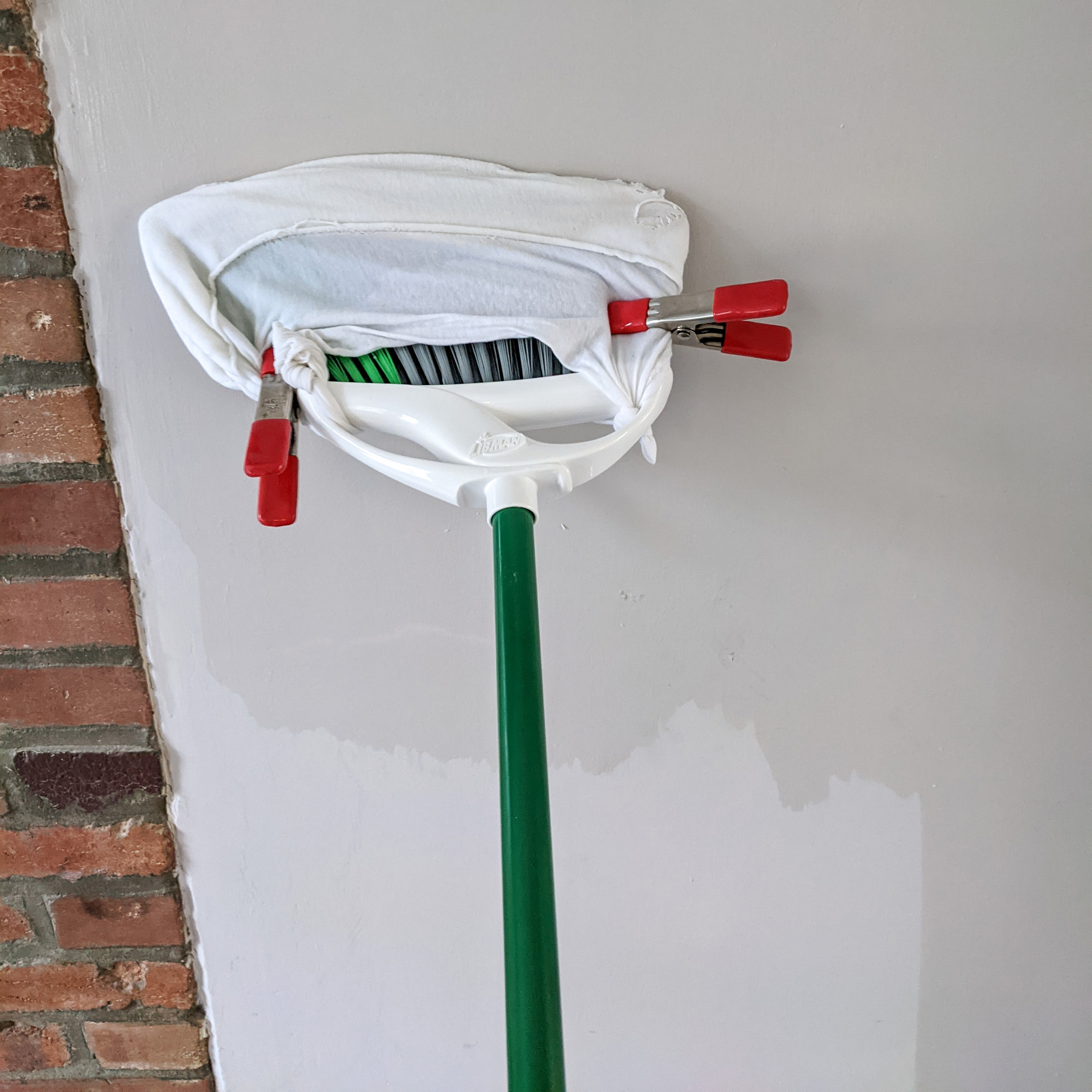 A wall being cleaned with a modified broom.