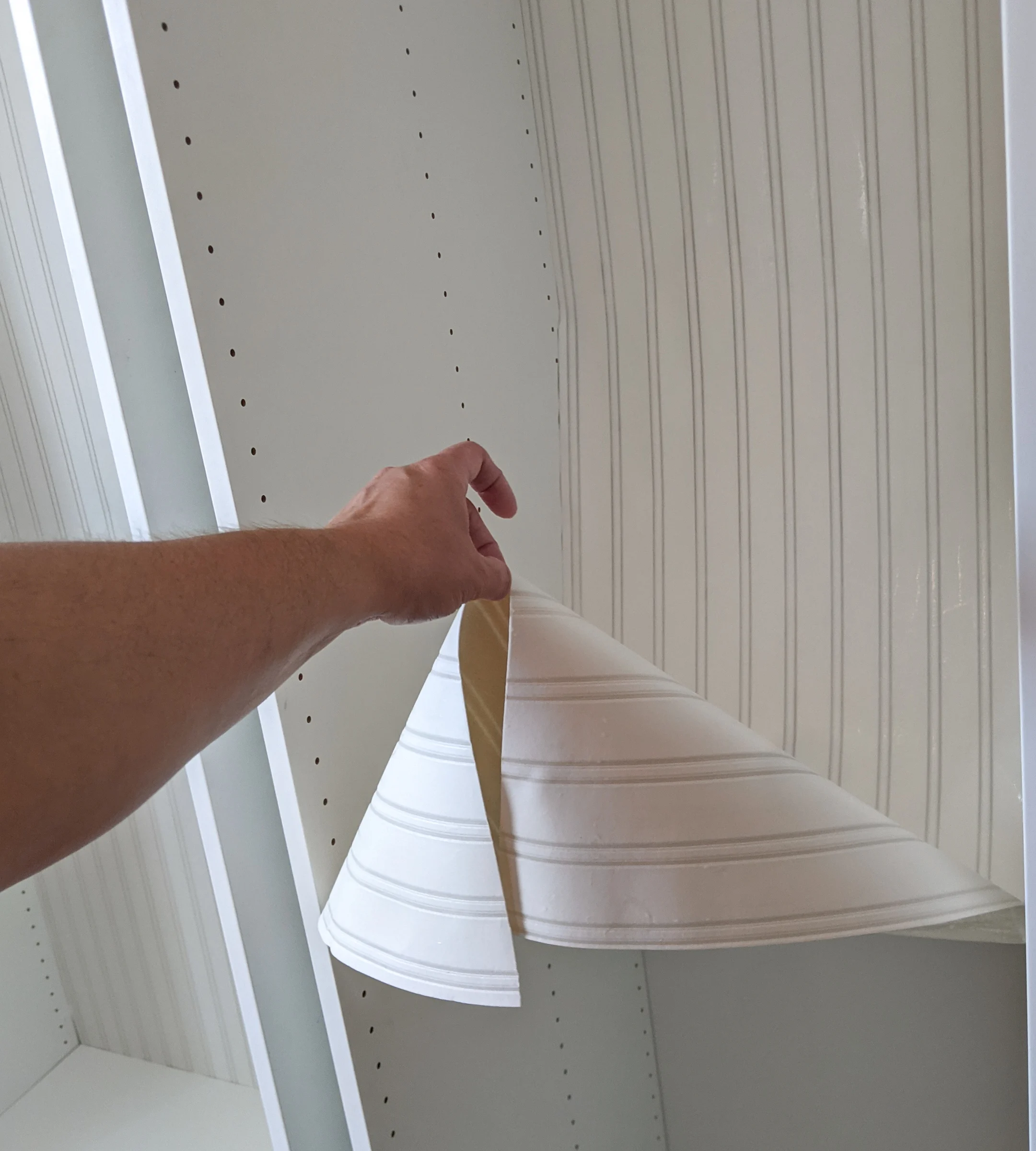 Bead board wallpaper being hung in an IKEA cabinet.