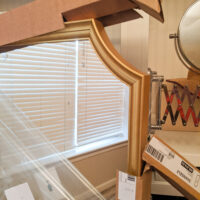 A partially unboxed ikea svansele mirror, with the gold frame peeking out of half removed cardboard packing.