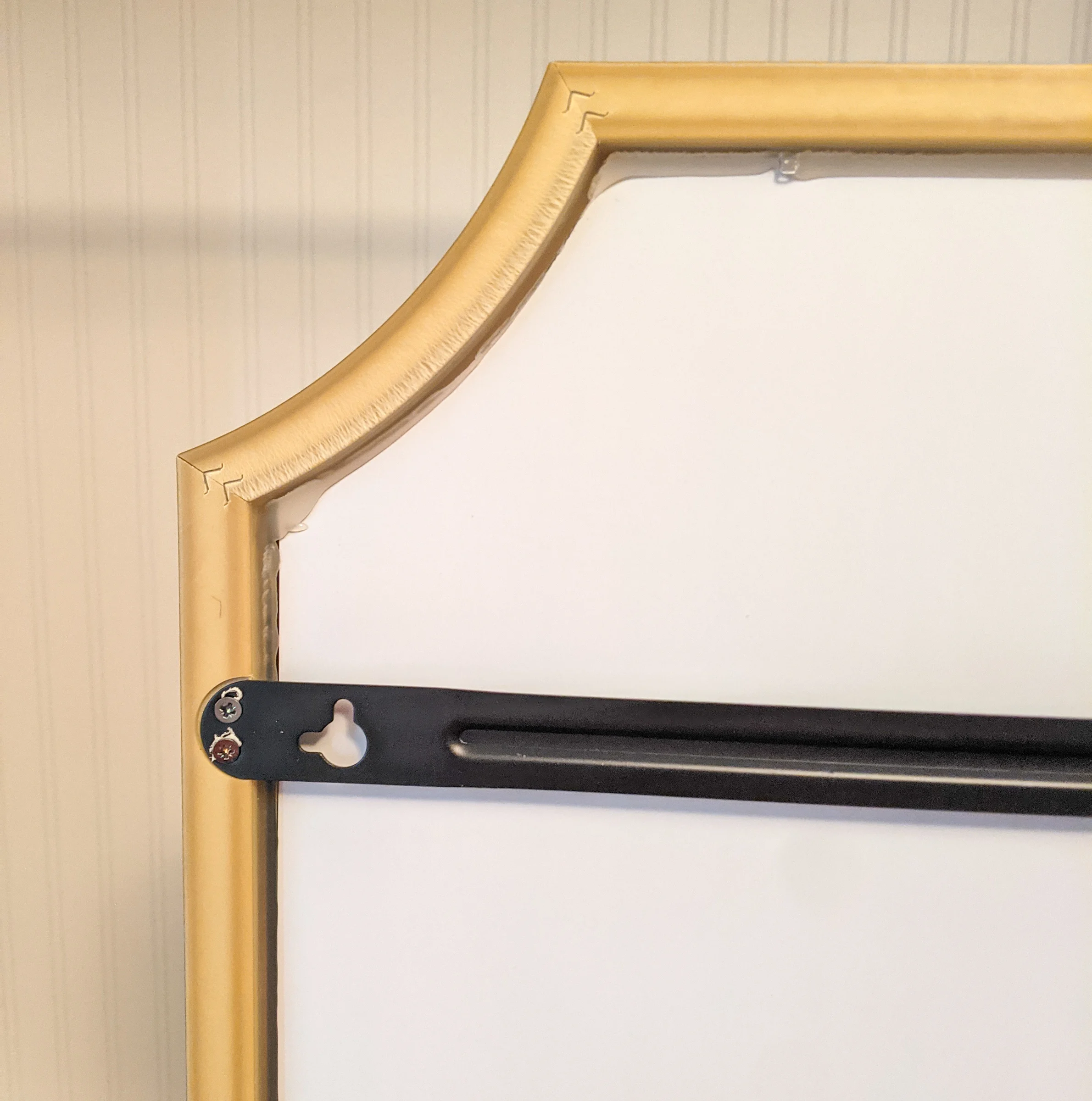 A close-up of the back side of the smear shows the support bars and hanging bracket, plus the back side of the frame and glue holding the mirror in the frame.