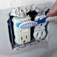 A toothbrush cleaning a dirty outlet with dust and grime in the crevices.