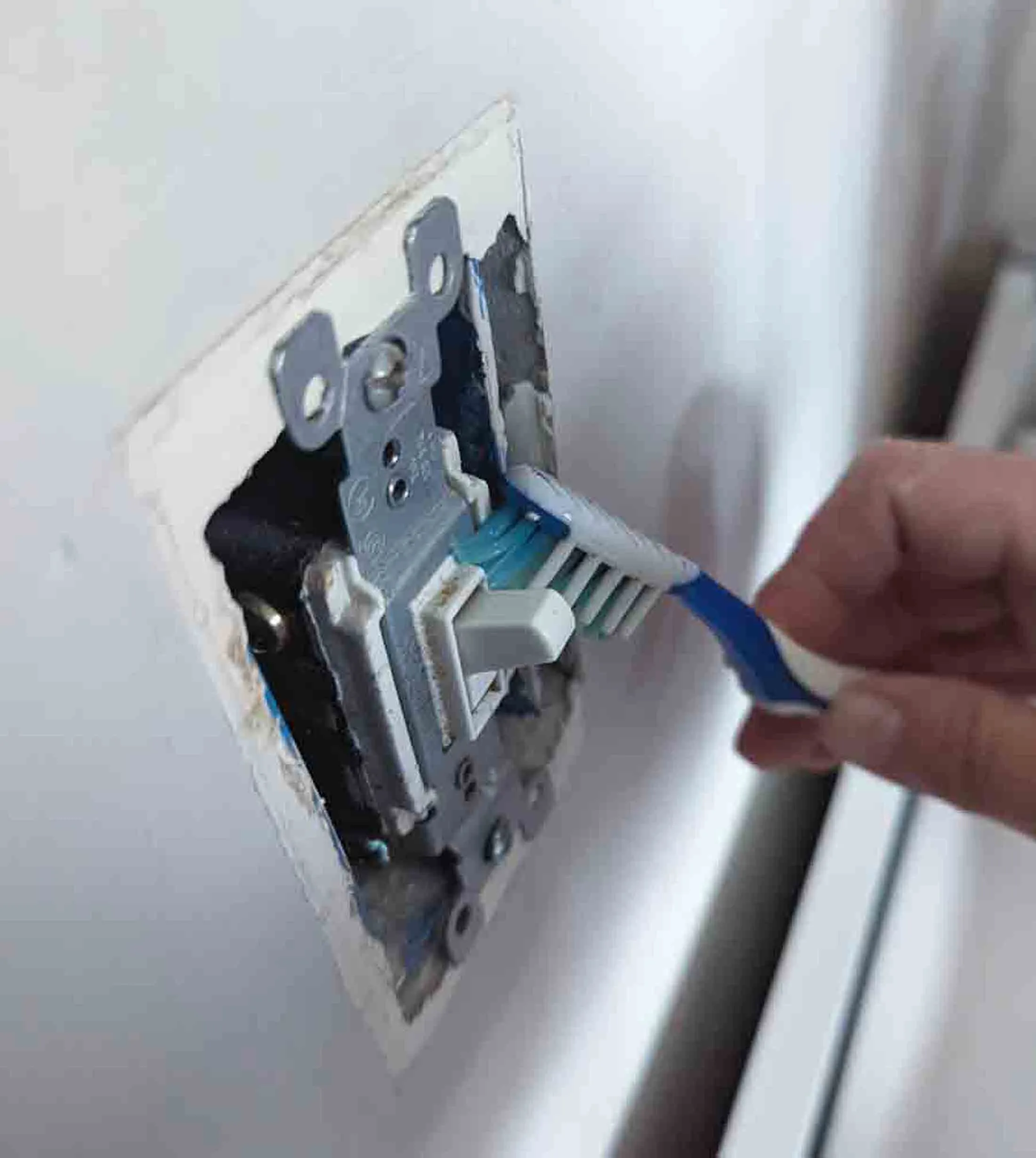 Cleaning a lightswitch using a toothbrush.