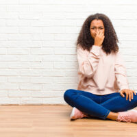 woman sitting on the floor holding nose.