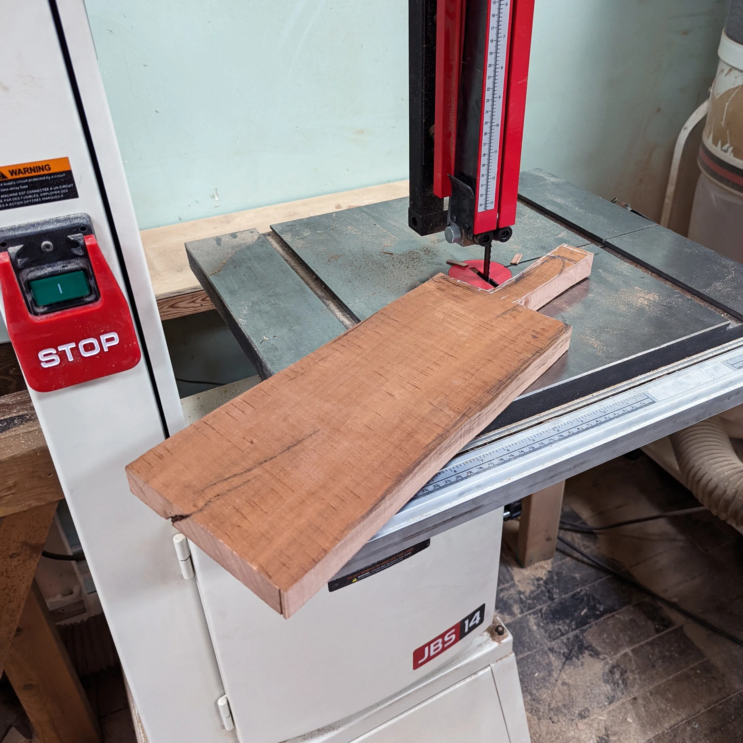 Cutting a plank of cherry wood into the shape of a cutting board using a large bandsaw in a community workshop in St. Louis.