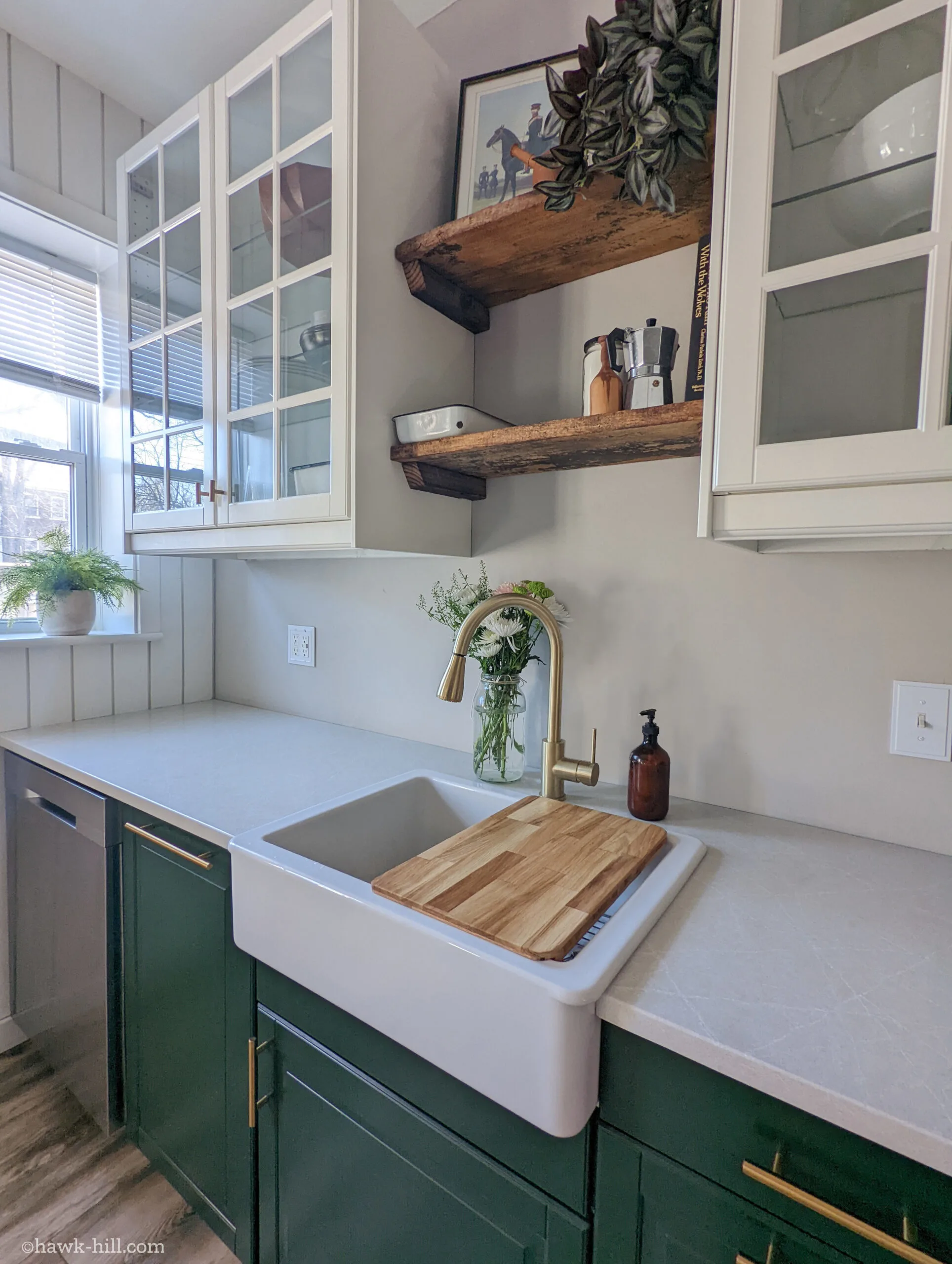 This IKEA kitchen features green cabinets, glass front white upper cabinets, and rustic open shelving created from reclaimed hundred-year-old wood planks.