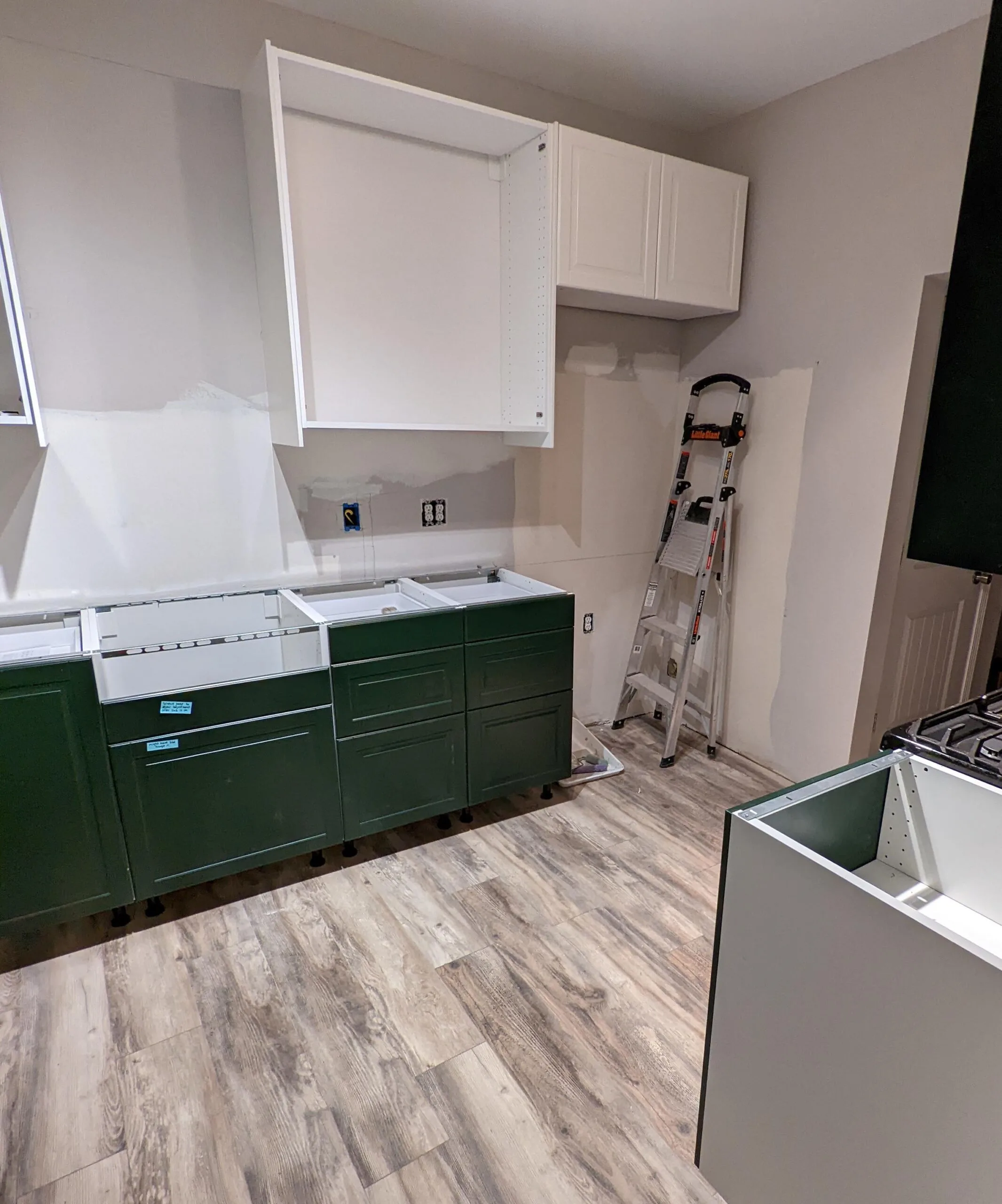 A green IKEA kitchen renovation in progress, shown with half finished cabinets and no appliances.