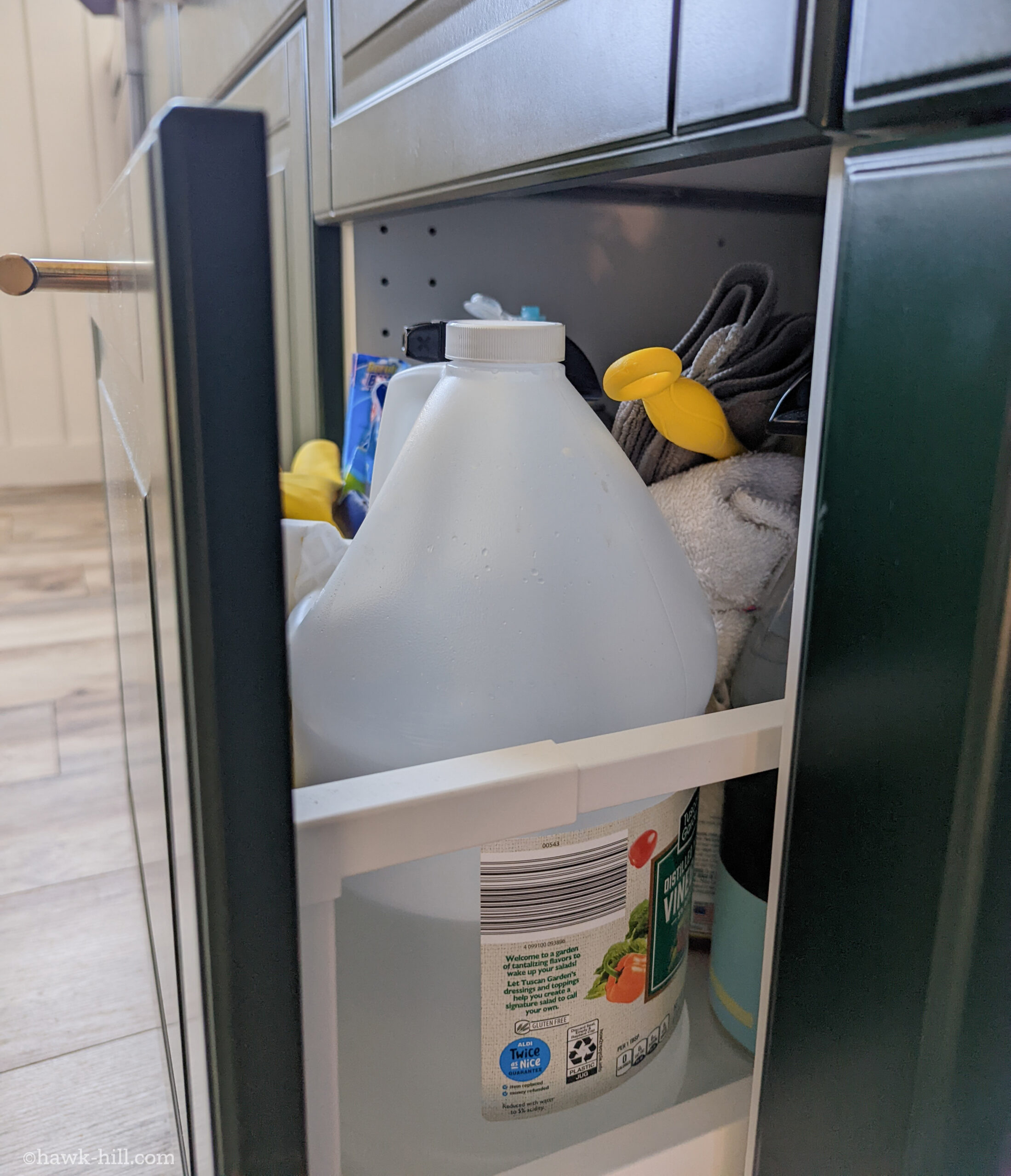 A drawer of cleaning supplies in a green IKEA kitchen.