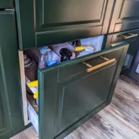 A drawer of cleaning supplies in a green IKEA kitchen.