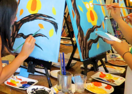partygoers paint owls on blue canvases at a paint and sip party.