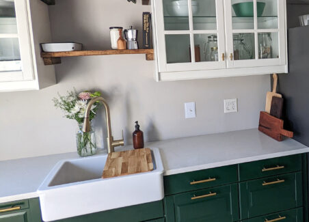 This kitchen renovation features forest green cabinets on the bottom and the combination of wood open shelving and glass front white cabinets on top.